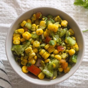 Indian corn chaat salad with yellow corn, cucumber, tomato, onion, coriander, and green chutney served in a bowl.