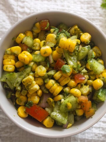 Indian corn chaat salad with yellow corn, cucumber, tomato, onion, coriander, and green chutney served in a bowl.