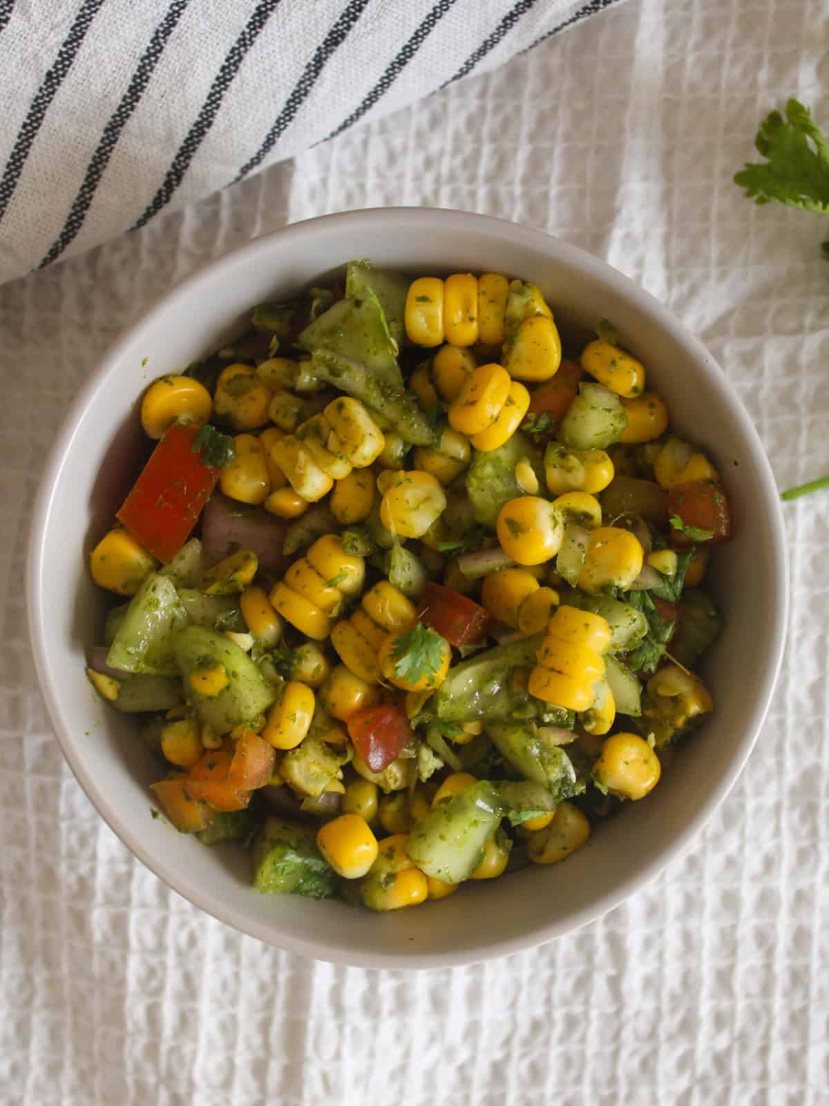 Top view of Indian corn chaat salad with steamed corn, cucumber, tomato, onion, and fresh coriander.