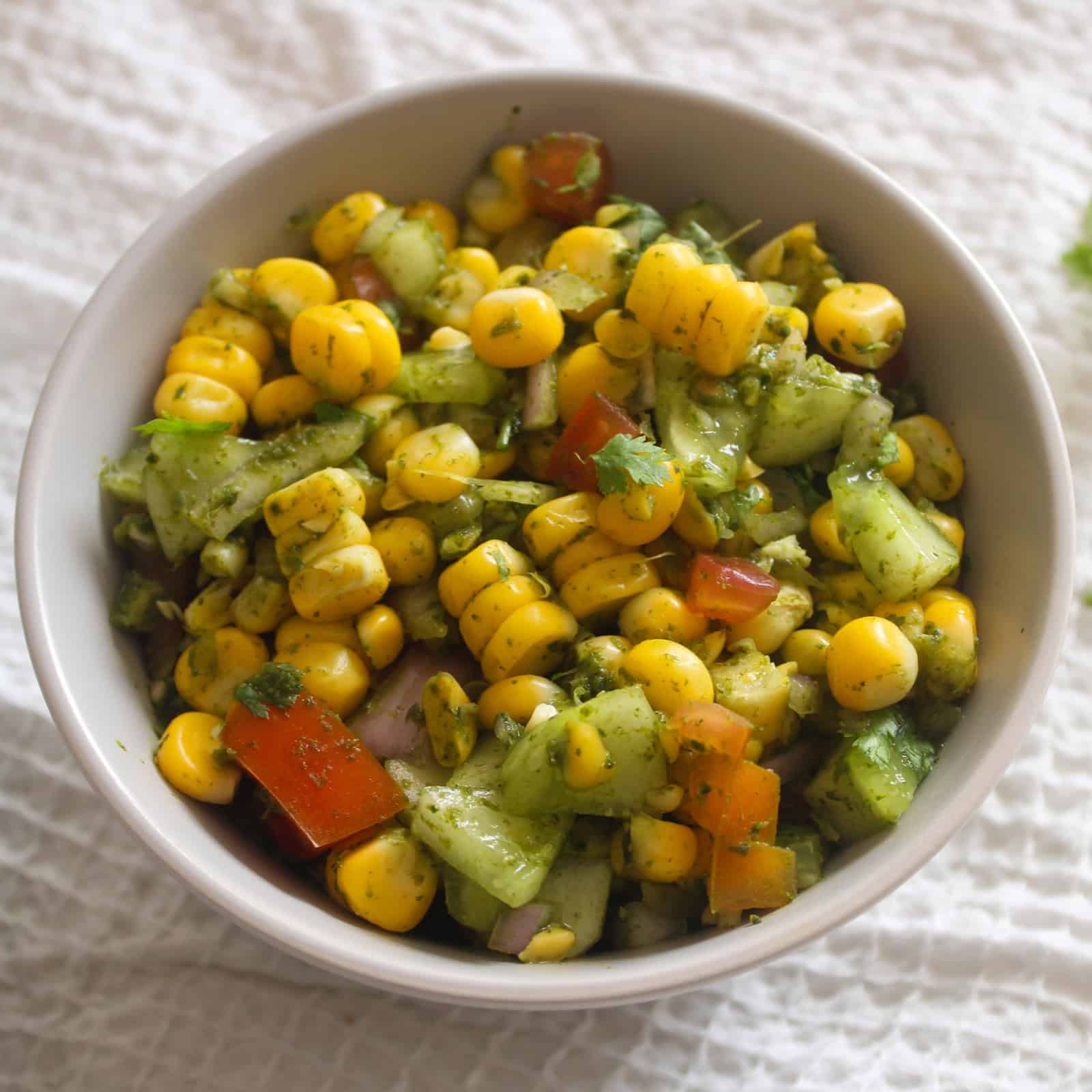 Close view of Indian corn chaat salad with bright corn, crisp cucumber, tomato, onion, coriander, and green chutney.