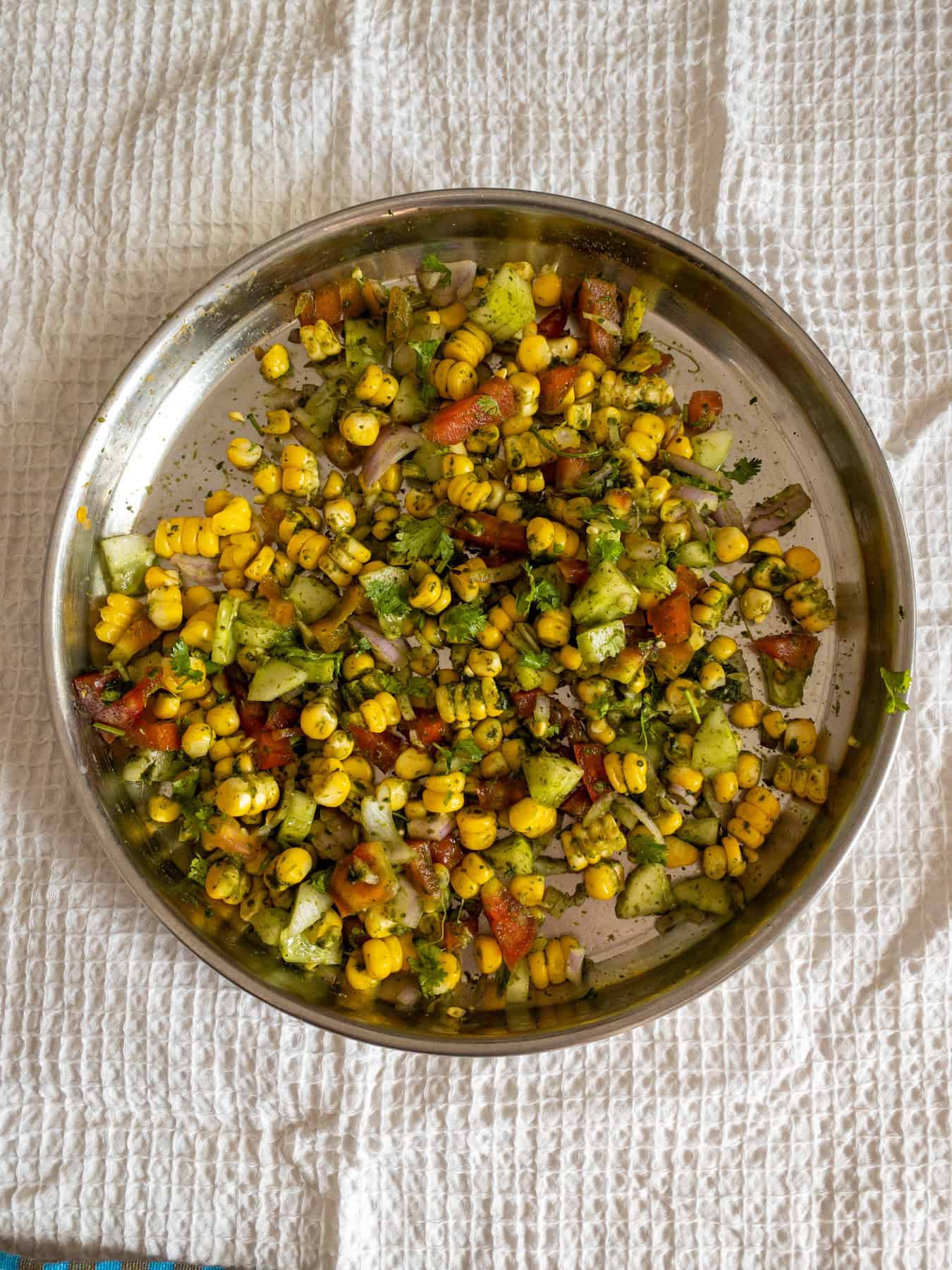 Steamed corn, cucumber, tomato, onion, and coriander tossed with green chutney in a steel plate.