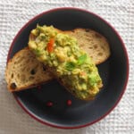 Chickpea avocado toast arranged over another toasted sourdough slice on a black plate.