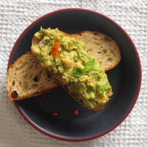 Chickpea avocado toast arranged over another toasted sourdough slice on a black plate.