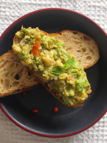Chickpea avocado toast arranged over another toasted sourdough slice on a black plate.