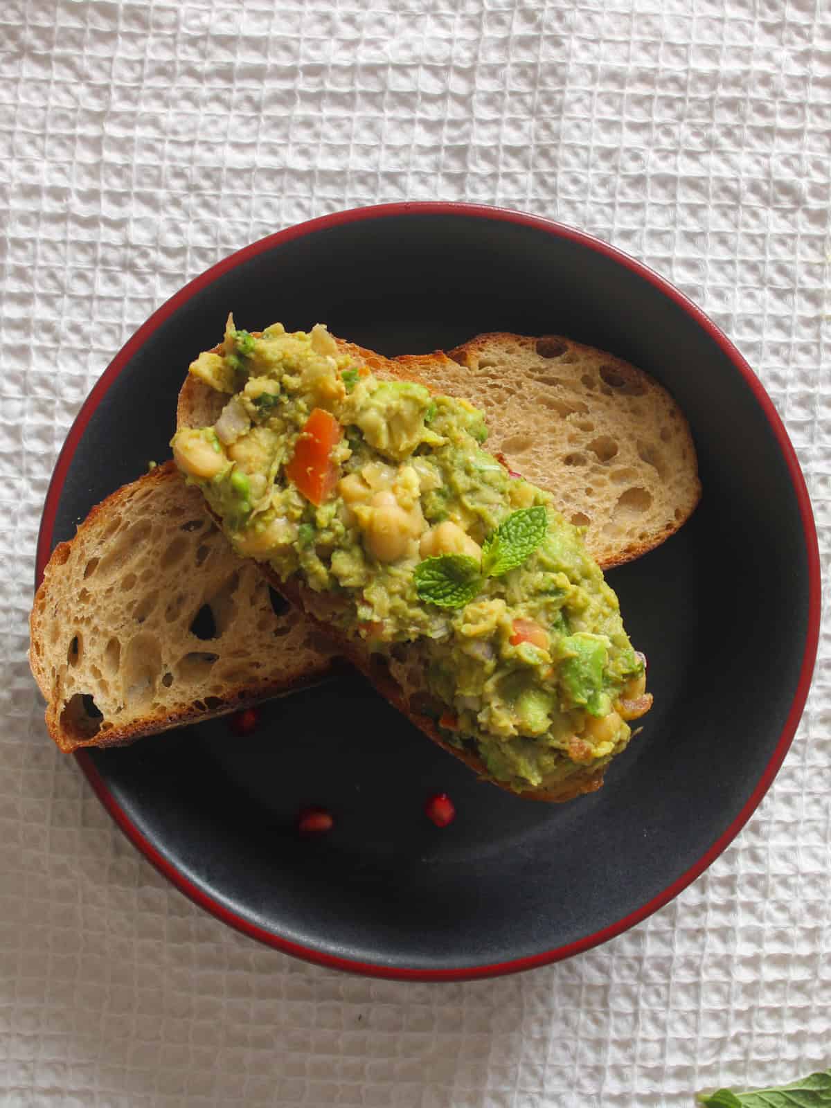 Chickpea avocado toast served with extra toasted sourdough on a black plate.