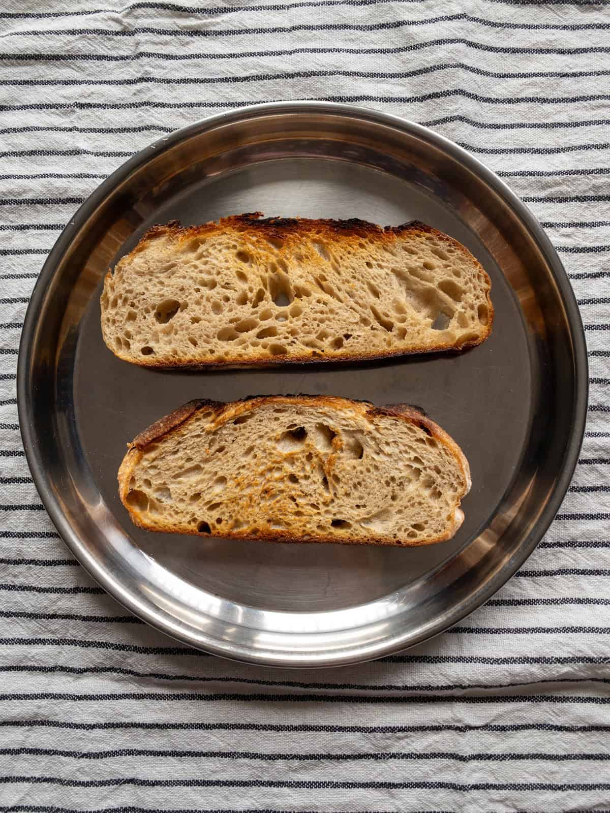 Two crisp sourdough bread slices arranged on a stainless steel plate.