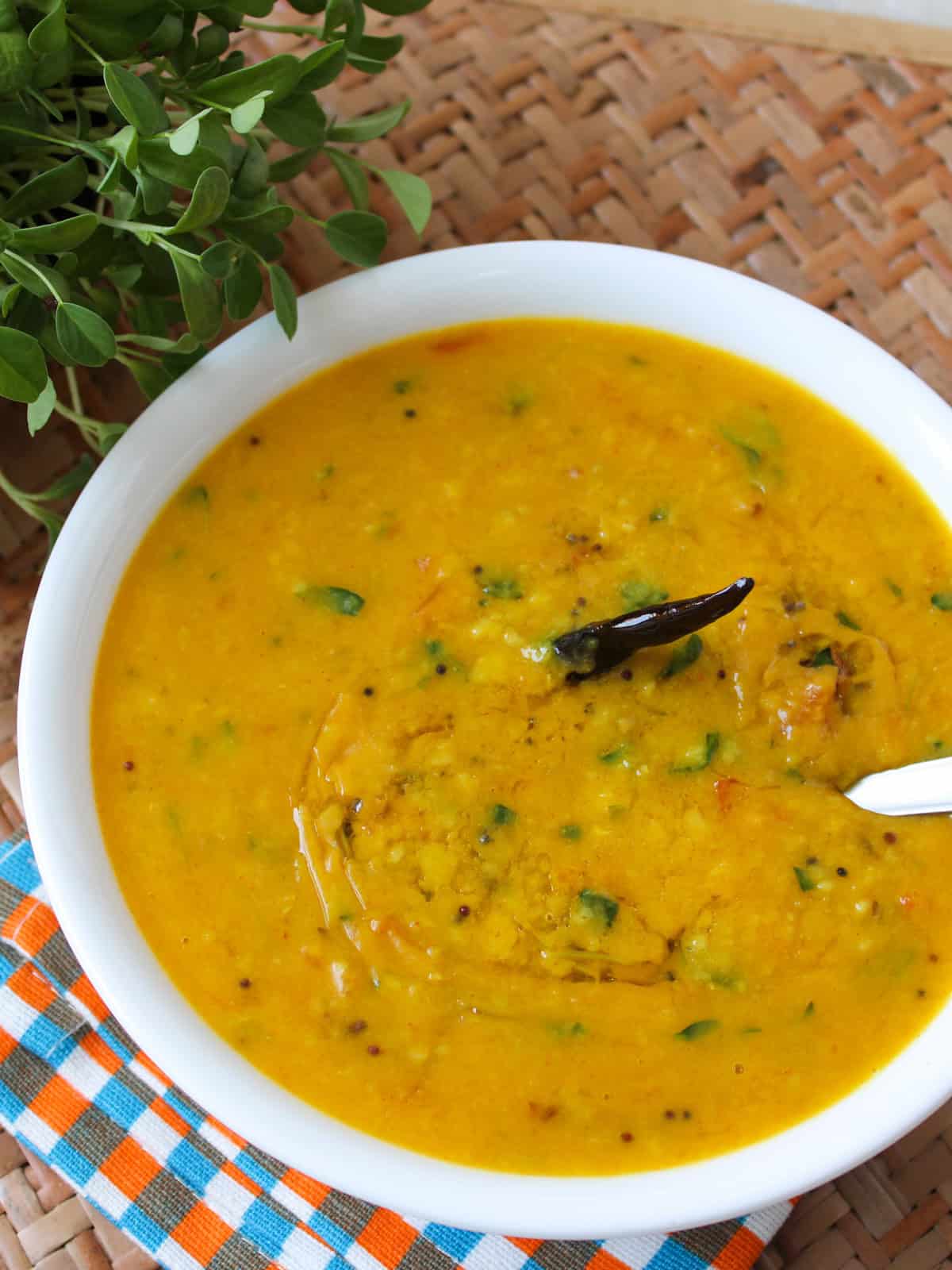Indian toor dal with fenugreek leaves, tomato, mustard seeds, and dried red chili served in a white bowl.