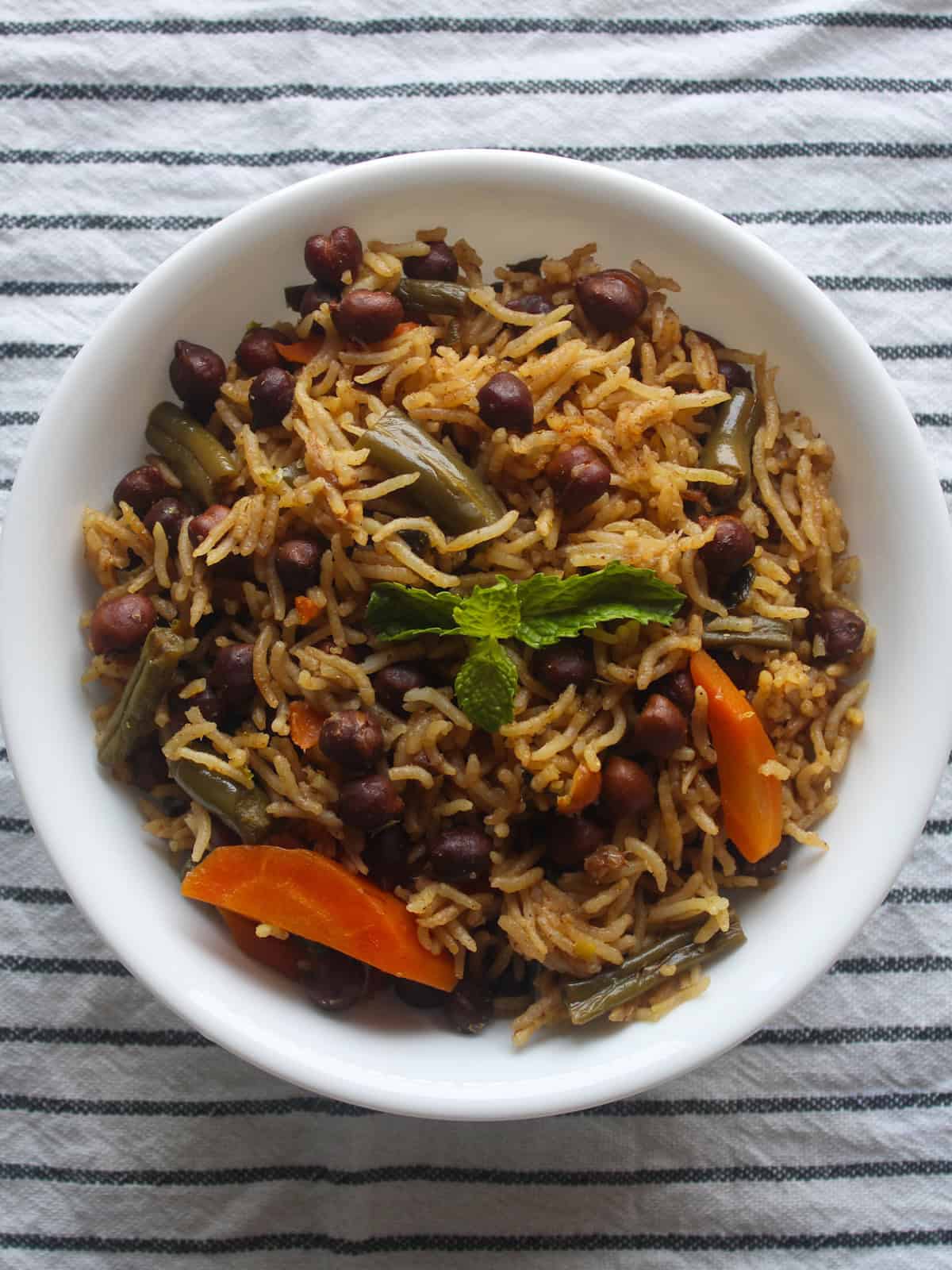Close view of kala chana pulao with basmati rice, black chickpeas, carrots, green beans, and mint.