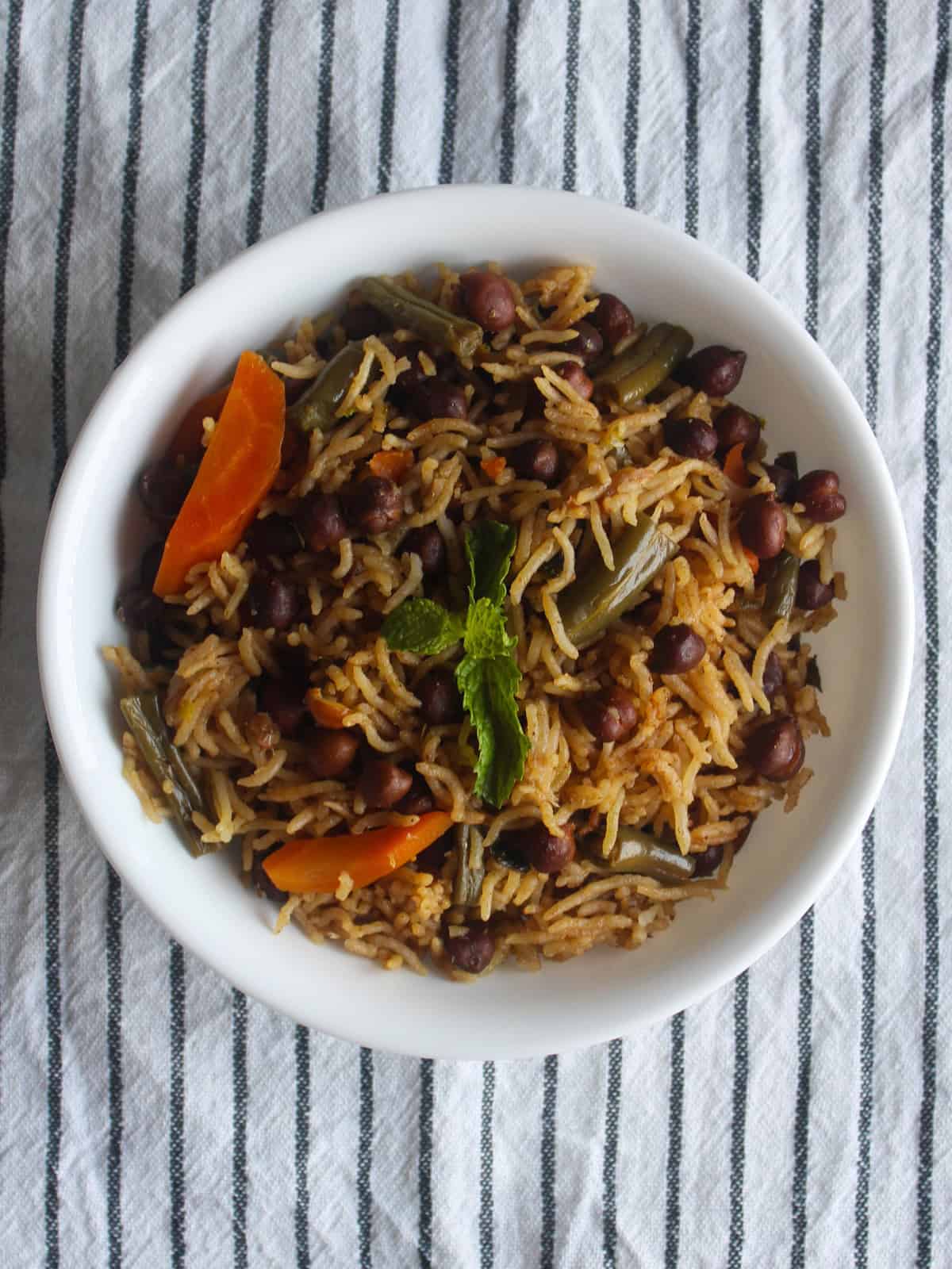 Kala chana pulao served in a white bowl with black chickpeas, carrots, green beans, and fresh mint.