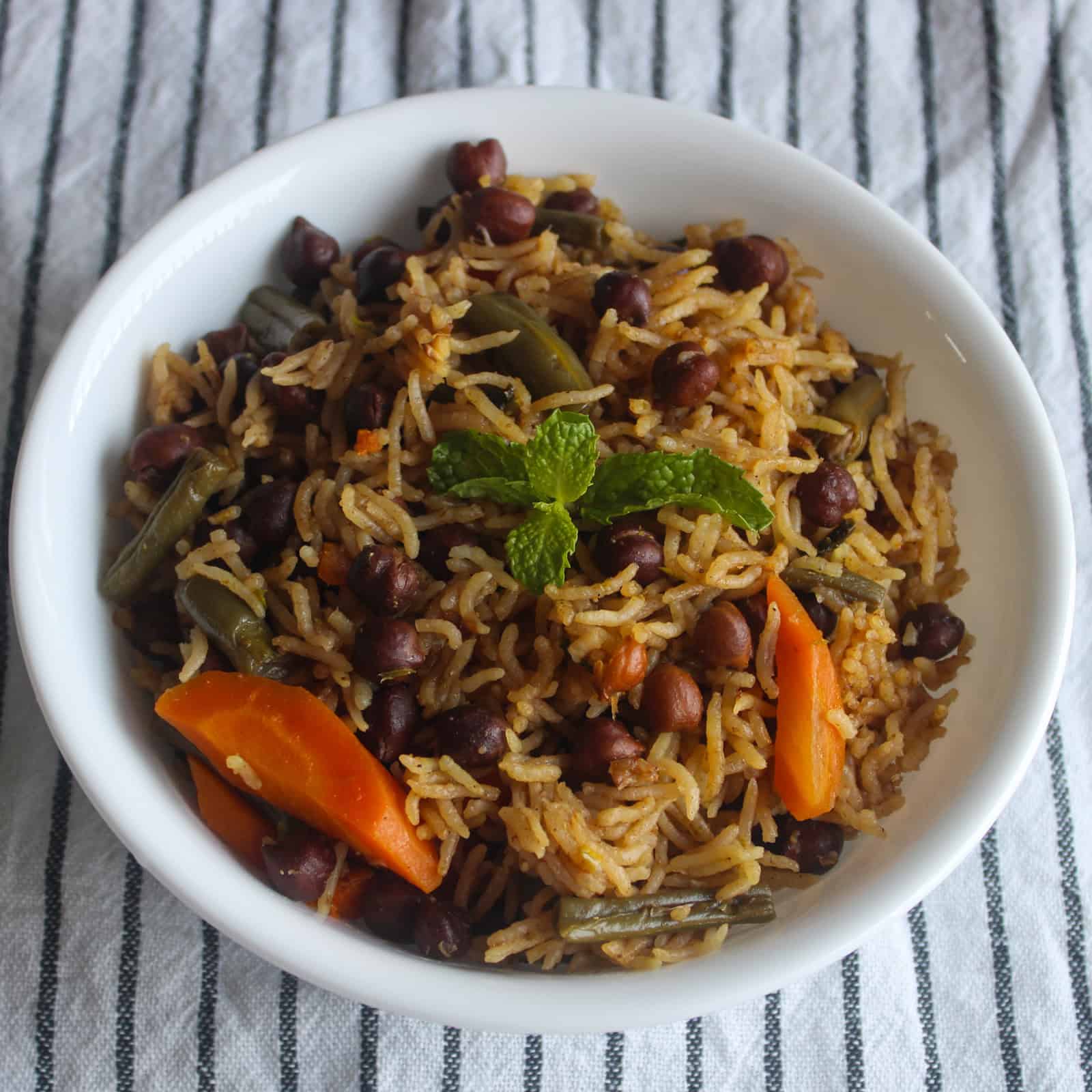 Kala chana pulao in a white bowl with black chickpeas, vegetables, and fresh mint garnish.