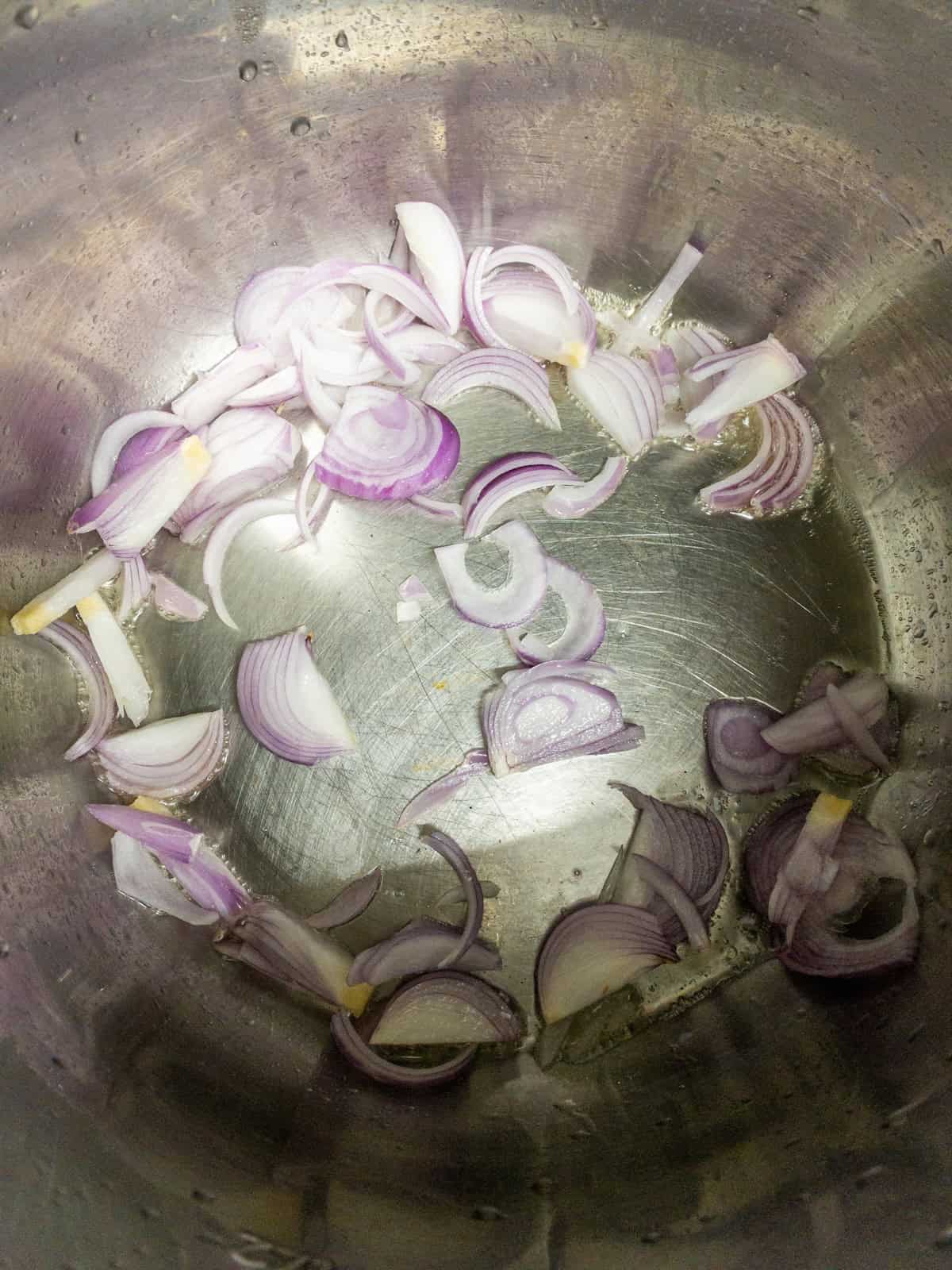 Sliced red onions starting to sautรฉ in oil inside the Instant Pot.