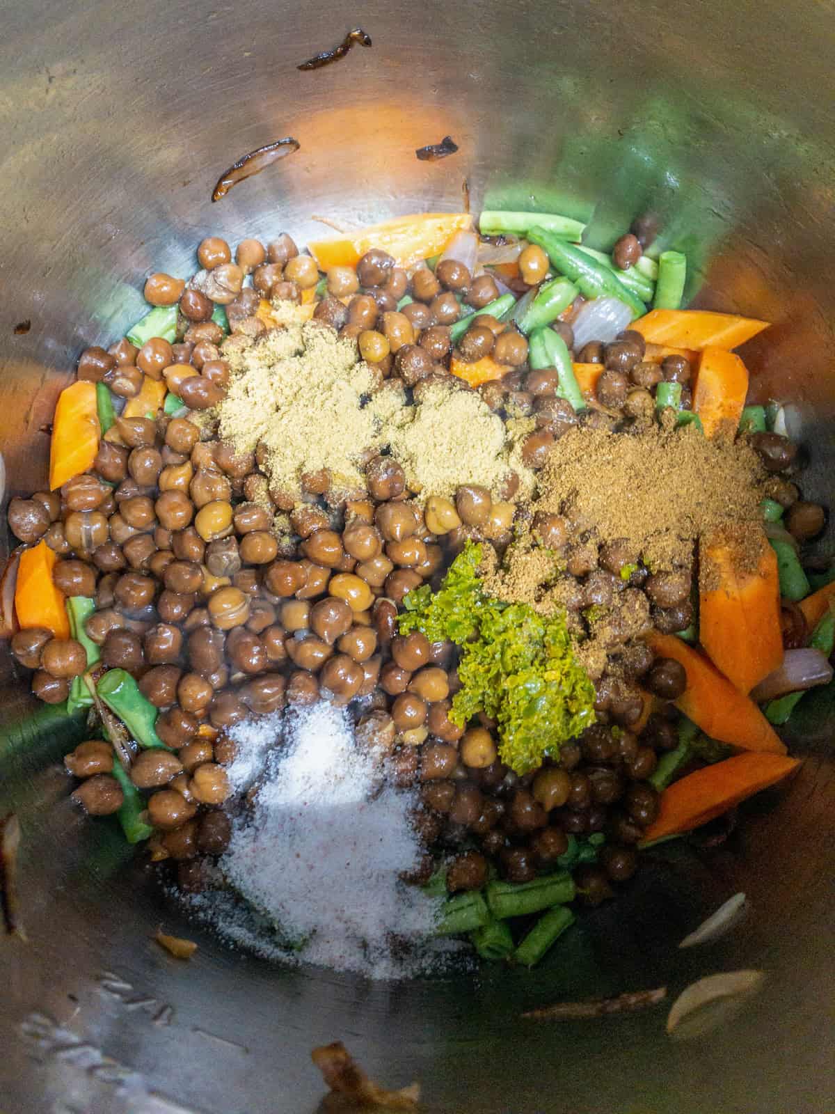 Cooked black chickpeas, carrots, green beans, salt, and ground spices in the pot.