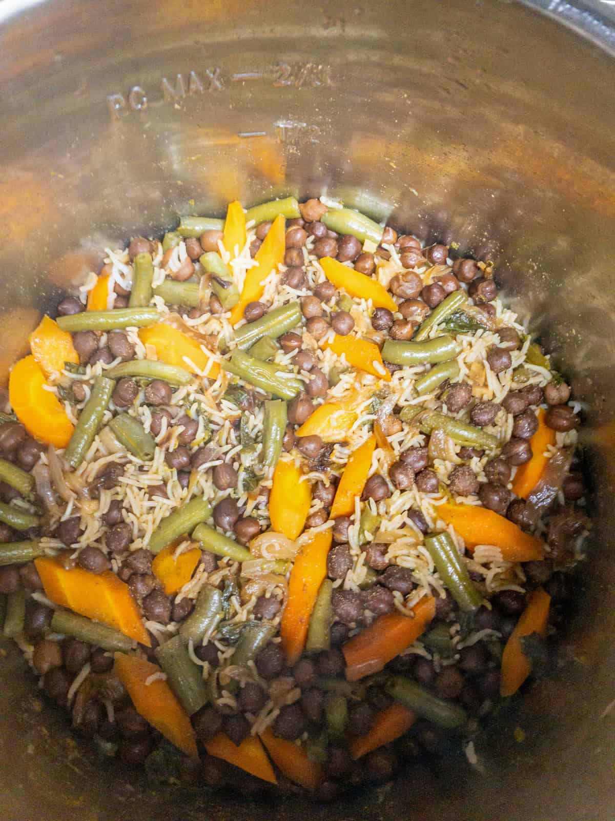 Basmati rice cooked with black chickpeas, carrots, and green beans inside the pot.