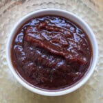 Glossy thick sweet tamarind chutney served in a white bowl on a textured golden plate.
