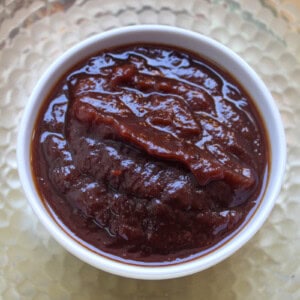 Glossy thick sweet tamarind chutney served in a white bowl on a textured golden plate.