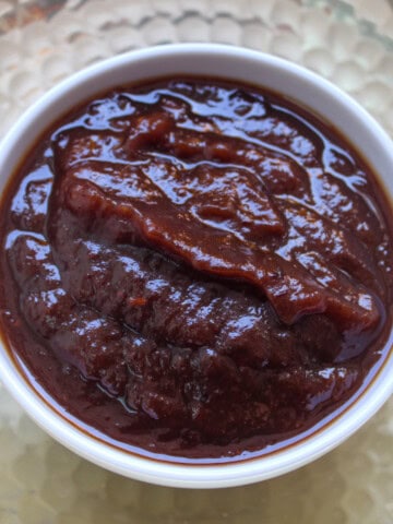 Glossy thick sweet tamarind chutney served in a white bowl on a textured golden plate.