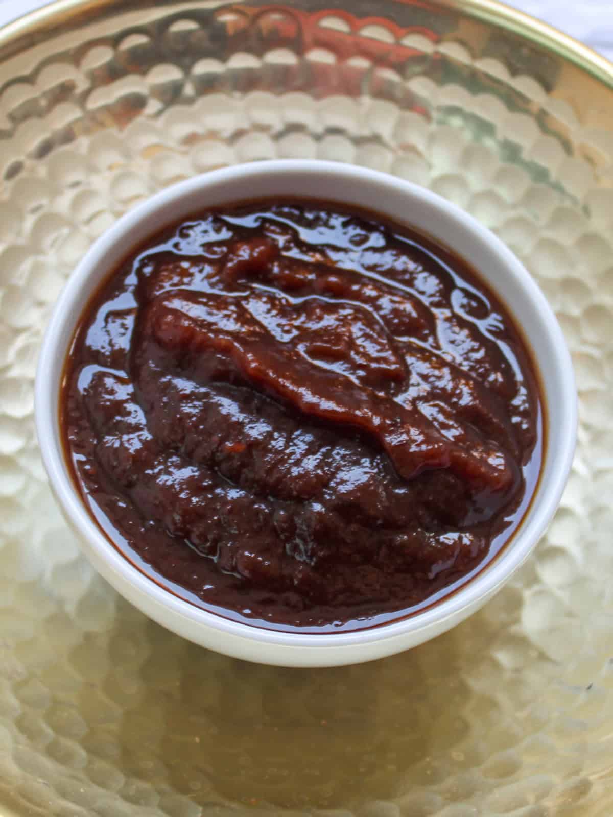Thick dark brown sweet tamarind chutney served in a small white bowl.