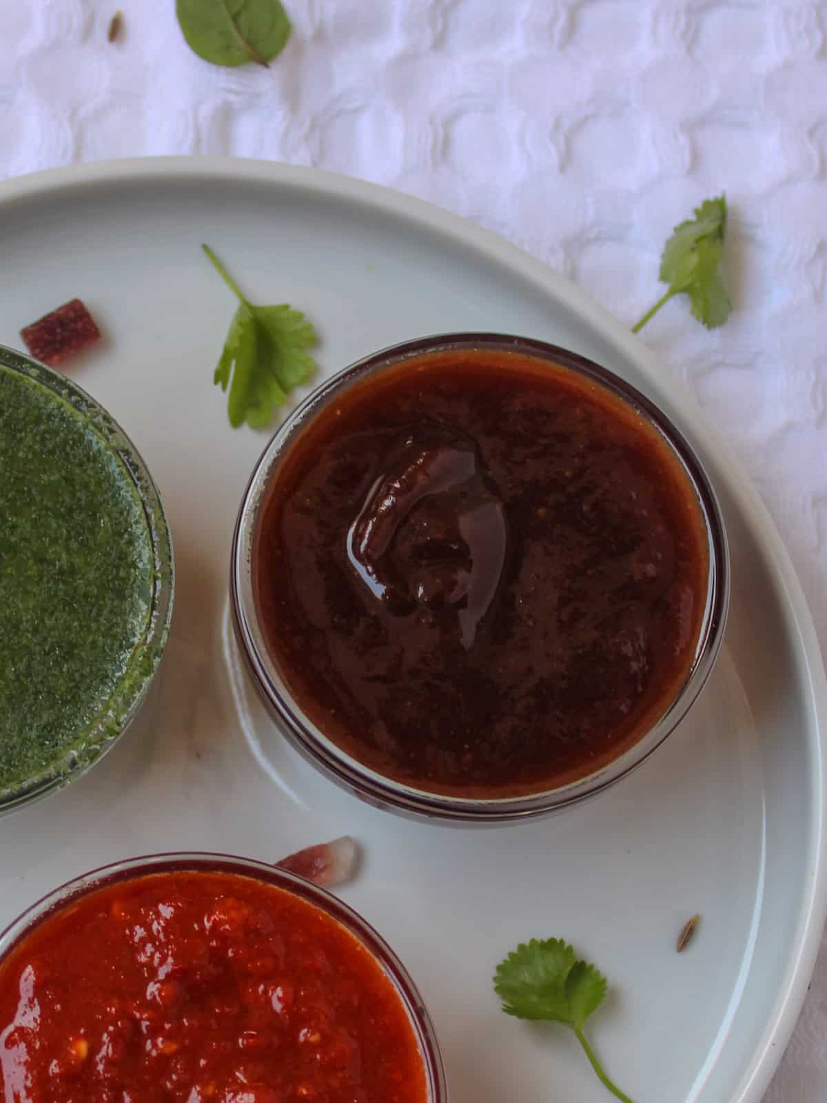 Sweet tamarind chutney arranged beside green and red chutneys on a white serving plate.