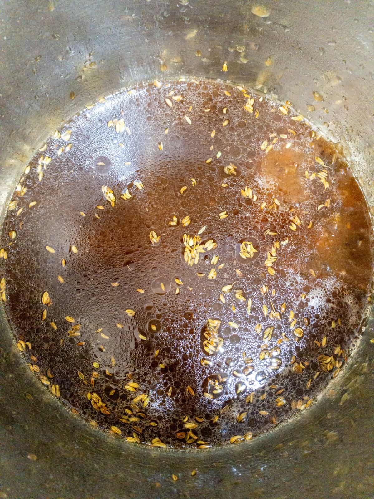 Dark tamarind mixture with fennel seeds in a stainless steel saucepan.