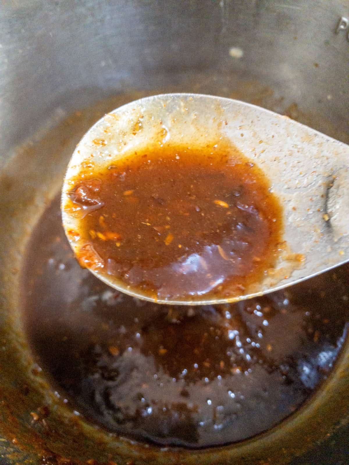 Thick sweet tamarind chutney coating a metal spoon above the saucepan.