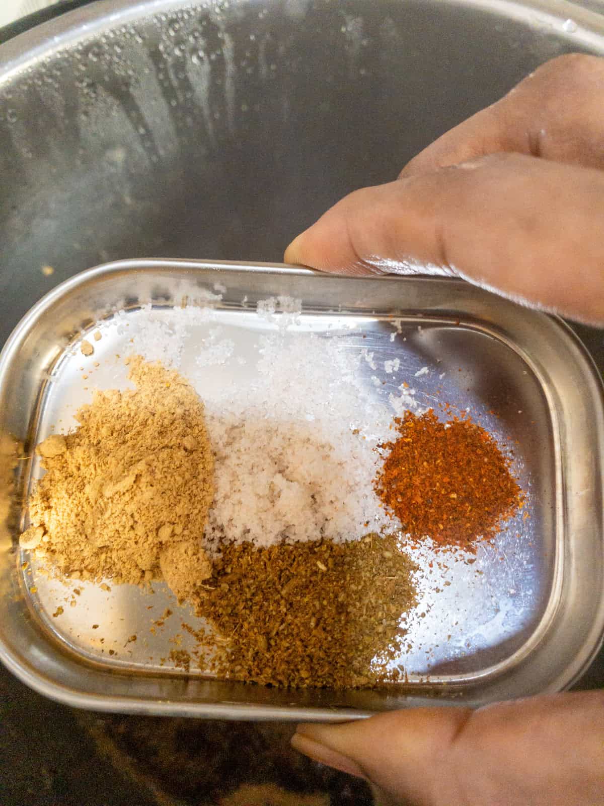 Salt, black salt, cumin powder, dry ginger powder, and red chili powder measured on a steel plate.