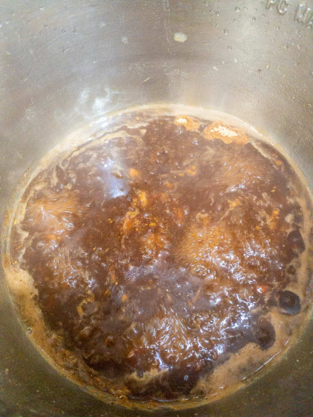Dark sweet tamarind chutney bubbling steadily as it simmers in a saucepan.