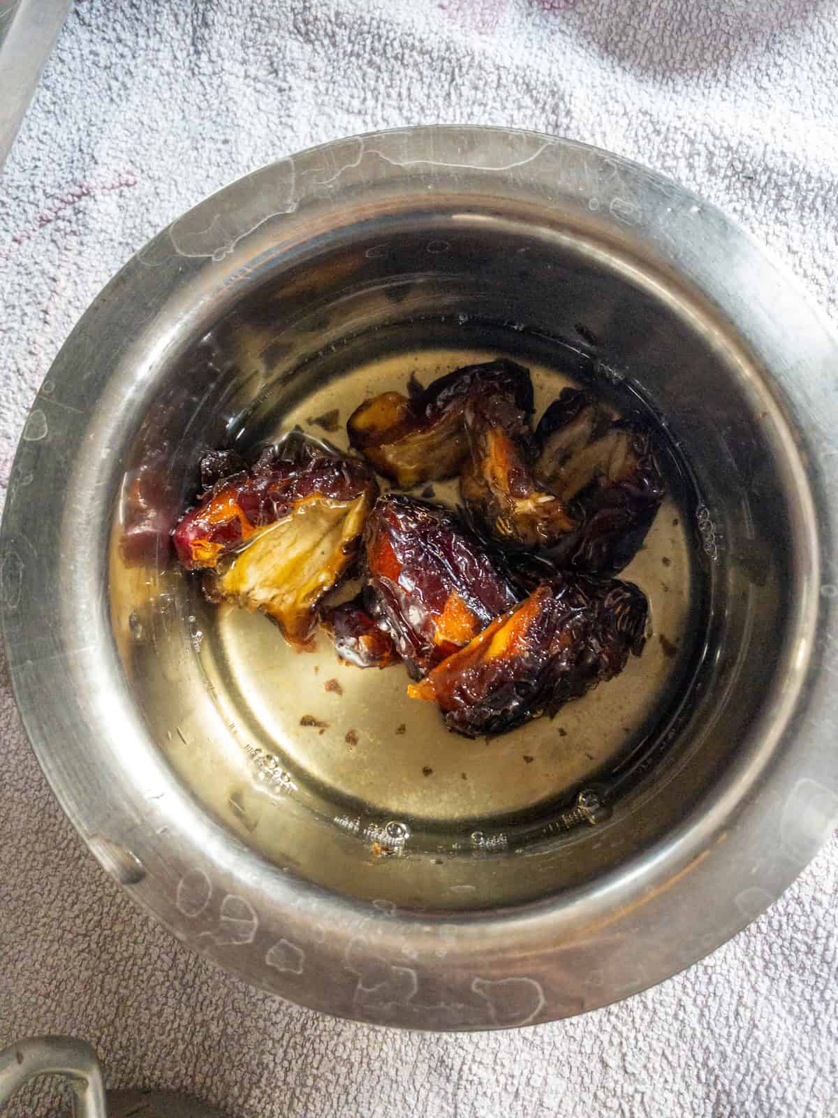 Dates soaking in water in a stainless steel bowl before cooking.