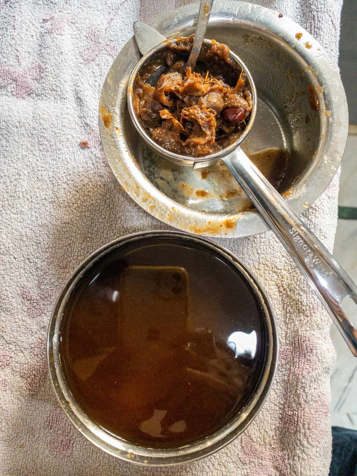 Softened tamarind pulp pressed through a metal sieve with dark tamarind liquid collected underneath.
