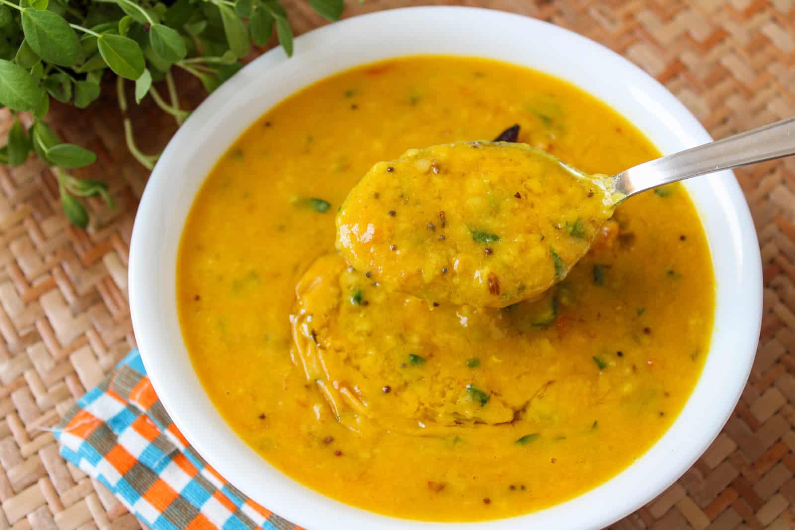 Close-up of a spoonful of thick toor dal with methi leaves and whole spices.